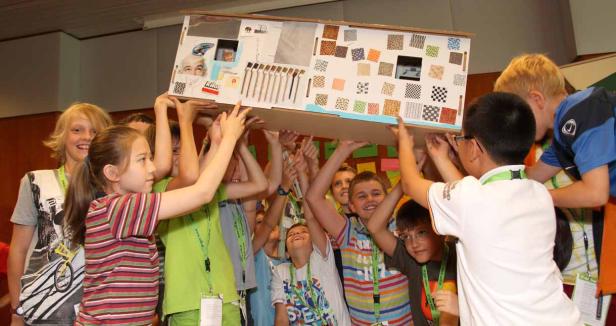 Eine Gruppe Kinder hält gemeinsam ein dekoriertes Papphaus hoch.