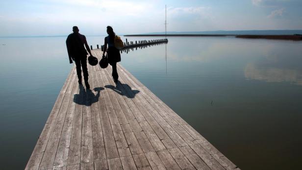 Badetauglich wird das Wetter über Pfingsten leider nicht. Zwei Personen gehen auf einem Holzsteg über einen ruhigen See.
