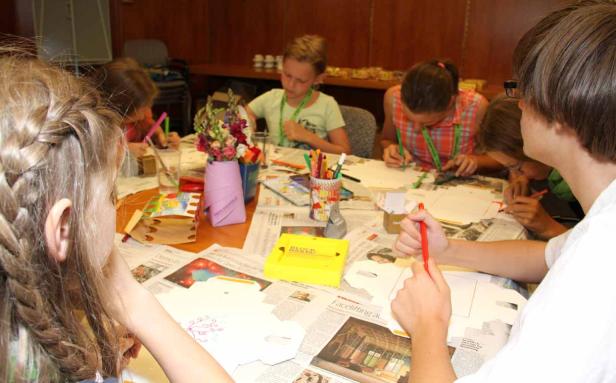 Eine Gruppe Kinder sitzt an einem Tisch und bastelt mit Stiften und Papier.