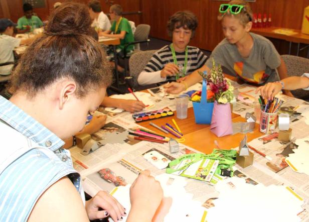 Kinder sitzen an einem Tisch und basteln mit Papier, Farben und Stiften.