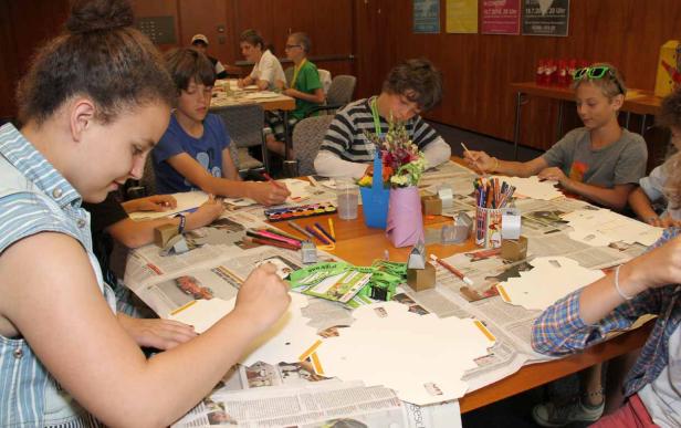 Eine Gruppe Kinder sitzt an einem Tisch und bastelt an Papierarbeiten.