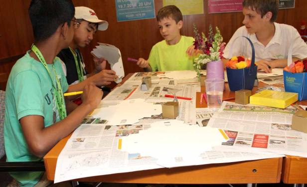 Eine Gruppe von Kindern bastelt an einem Tisch mit Papier und Scheren.