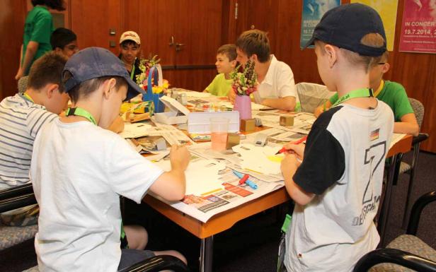 Eine Gruppe Kinder sitzt an einem Tisch und bastelt mit Papier und Stiften.