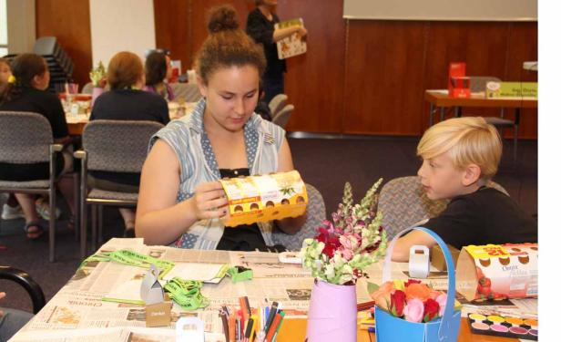 Eine junge Frau und ein Junge basteln an einem Tisch mit Zeitungen und Blumen.