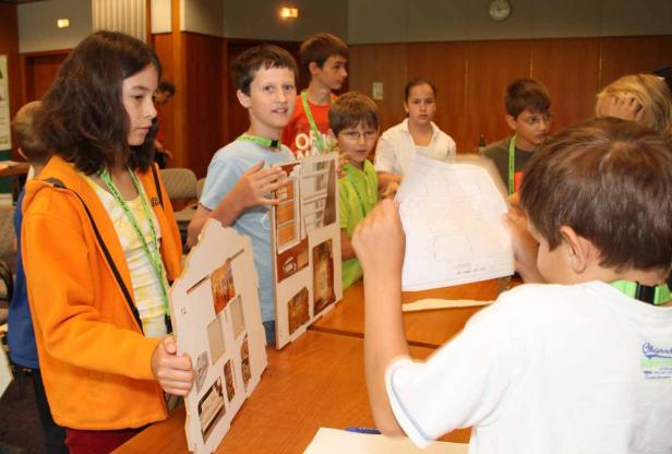 Eine Gruppe Kinder arbeitet an einem Projekt mit Hausmodellen und Bauplänen.
