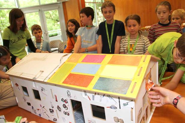 Eine Gruppe Kinder und eine Frau betrachten und dekorieren ein Modellhaus.