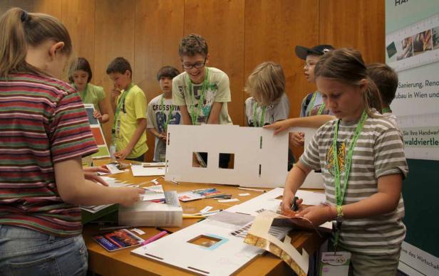 Eine Gruppe Kinder bastelt an einem Tisch mit Papier und Scheren.