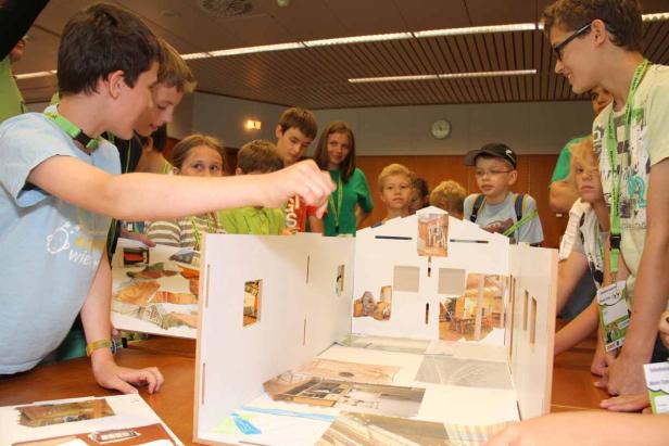 Eine Gruppe Kinder bastelt an einem Modellhaus mit ausgeschnittenen Bildern.