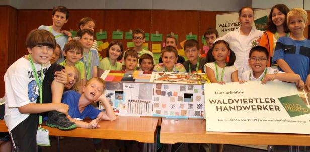 Eine Gruppe Kinder präsentiert ein Modellhaus und ein Schild von Waldviertler Handwerker.