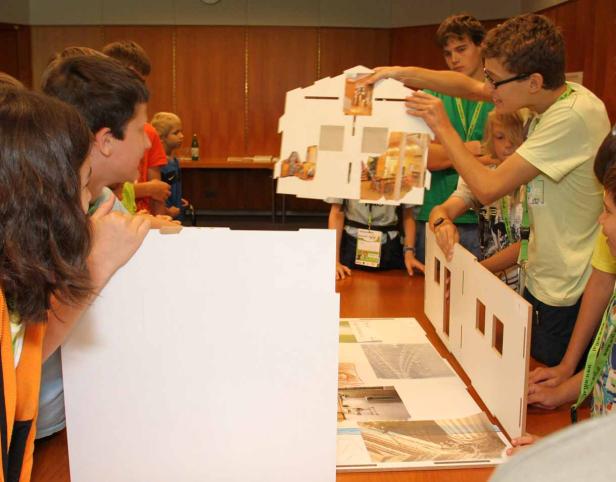 Eine Gruppe von Kindern arbeitet an einem Modellhaus mit Fotos an einem Tisch.