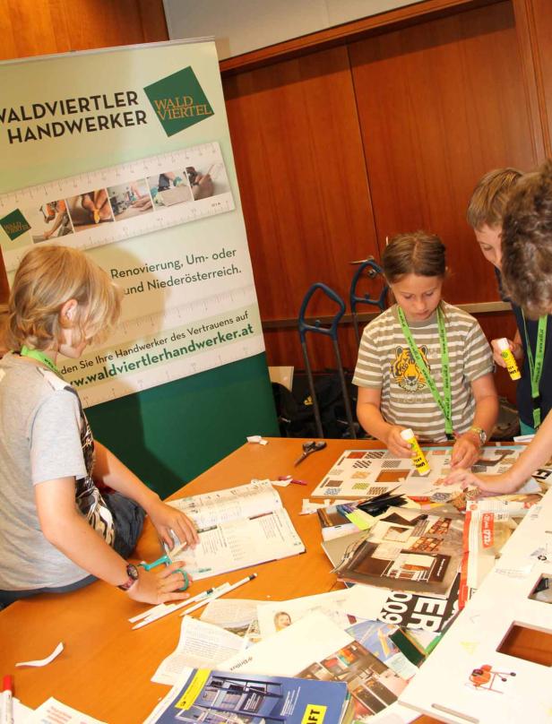 Kinder basteln an einem Tisch mit Zeitschriften und Klebstoff, im Hintergrund ein Banner von Waldviertler Handwerker.