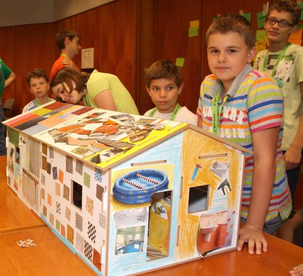 Eine Gruppe Kinder betrachtet ein selbstgebautes und dekoriertes Puppenhaus.
