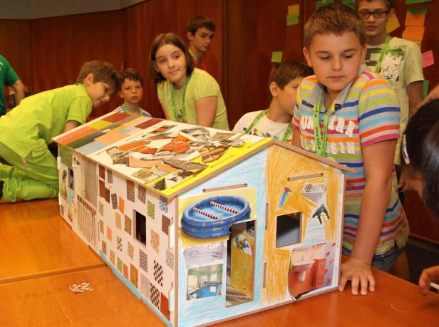 Eine Gruppe Kinder betrachtet ein selbstgebautes, dekoriertes Hausmodell.