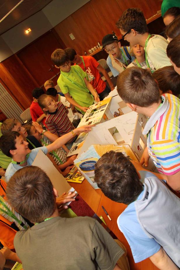 Eine Gruppe Kinder betrachtet ein Modellhaus auf einem Tisch.