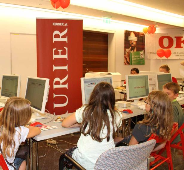 Kinder sitzen an Computern vor einem Banner von Kurier.at.