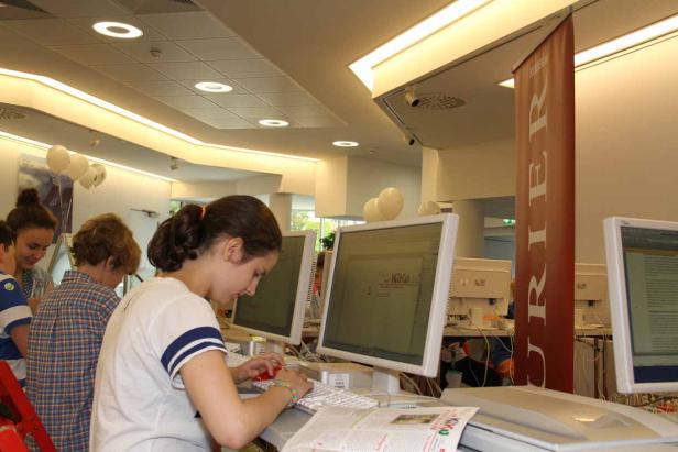Eine junge Frau tippt an einem Computer in einem hellen Raum mit anderen Personen und Ballons.