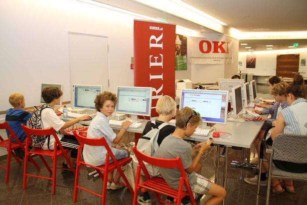 Eine Gruppe Kinder sitzt an Computern in einem hellen Raum.