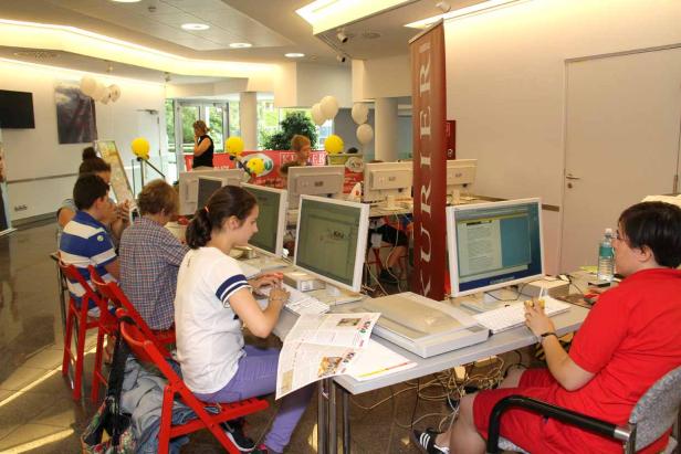 Mehrere Personen sitzen an Computern in einem hellen Raum.