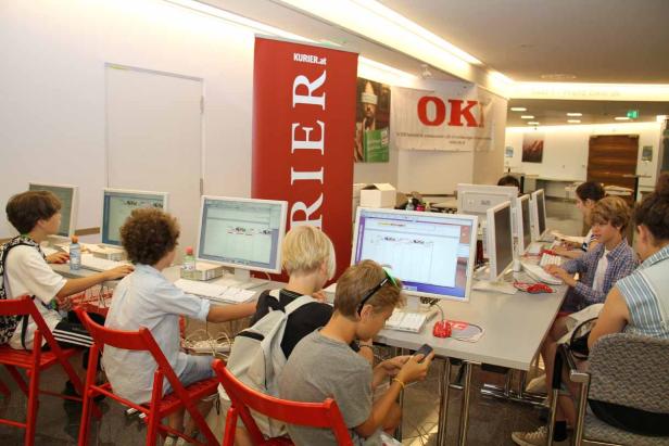 Eine Gruppe von Kindern sitzt an Computern in einem Raum mit einem „Kurier.at“-Banner.