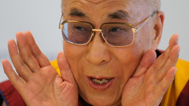 Der Dalai Lama lächelt und hält seine Hände vor sein Gesicht.