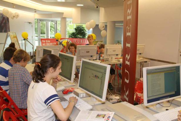 Kinder sitzen an Computern in einem Raum mit einem „Kurier“-Banner.