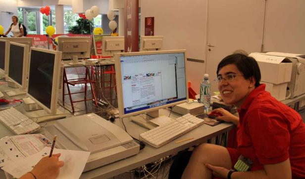 Eine Frau sitzt an einem Computer in einem Büro mit dem KIKU-Logo auf dem Bildschirm.