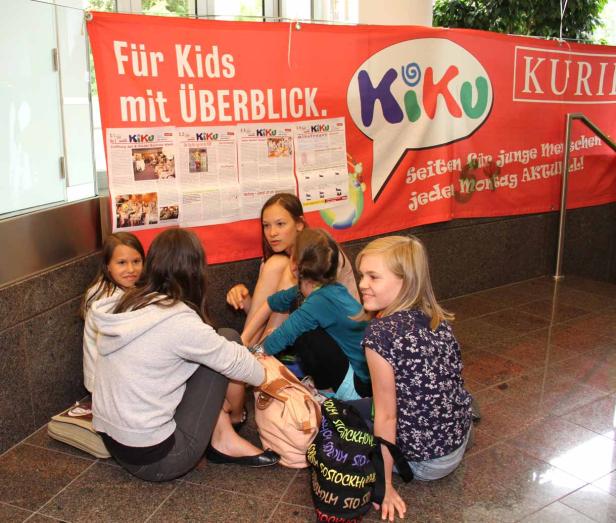 Eine Gruppe Mädchen sitzt vor einem Banner mit der Aufschrift „Für Kids mit ÜBERBLICK“.