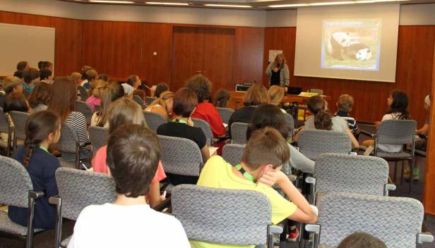 Eine Frau hält einen Vortrag vor einer Gruppe von Kindern; auf der Leinwand sind Pandas zu sehen.