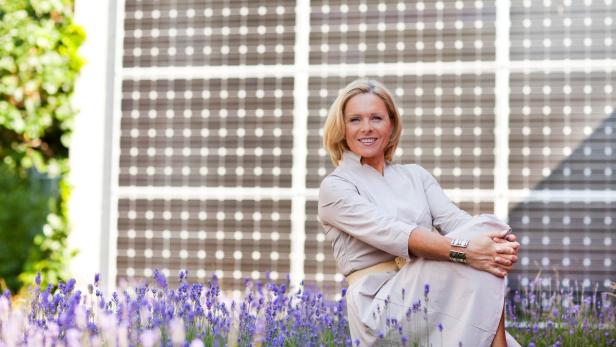 Eine Frau sitzt vor einer Wand aus Solarzellen in einem Feld mit lila Lavendelblüten.
