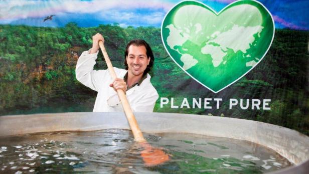 Ein Mann im Laborkittel rudert in einem großen Wasserbecken vor einem „Planet Pure“-Hintergrund.