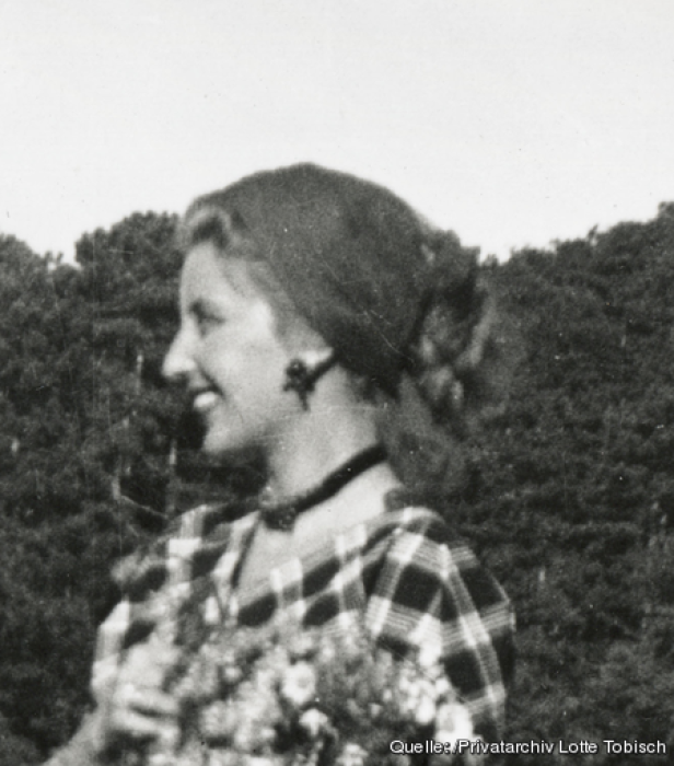 Eine lächelnde Frau mit Kopftuch und Blumenstrauß, aufgenommen im Profil.