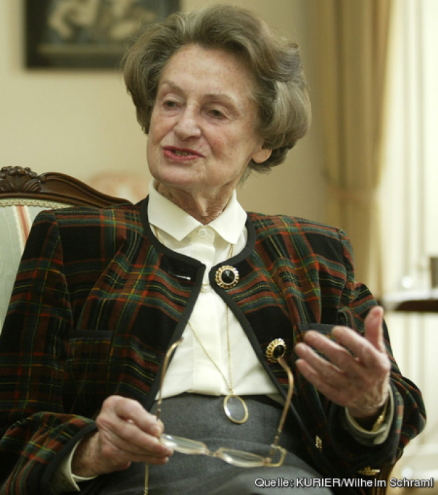 Eine ältere Frau mit Brille gestikuliert während eines Gesprächs.