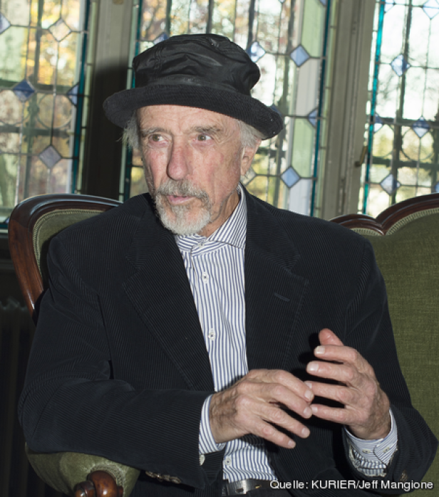 Ein älterer Mann mit Hut und Anzug sitzt in einem Sessel.