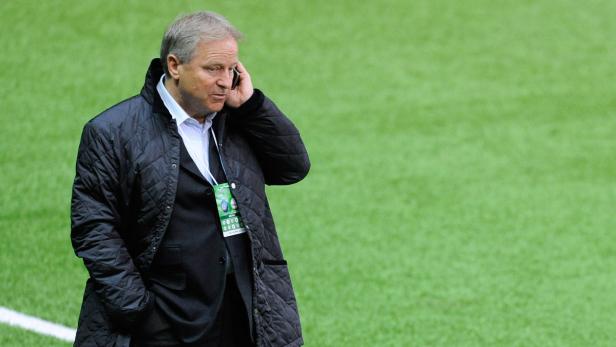 Ein Mann in Jacke telefoniert auf einem grünen Feld.