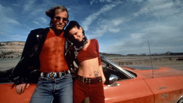 Woody Harrelson und Juliette Lewis posieren an einem roten Auto in der Wüste für „Natural Born Killers“.