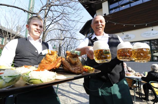 Zwei Kellner servieren Haxen und Bier in einem Biergarten.