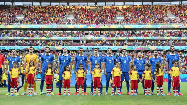 Die griechische Fußballnationalmannschaft steht mit jungen Fans vor einem Spiel auf dem Rasen.