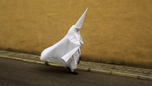 Eine Person in einem weißen Gewand und spitzem Hut geht die Straße entlang.
