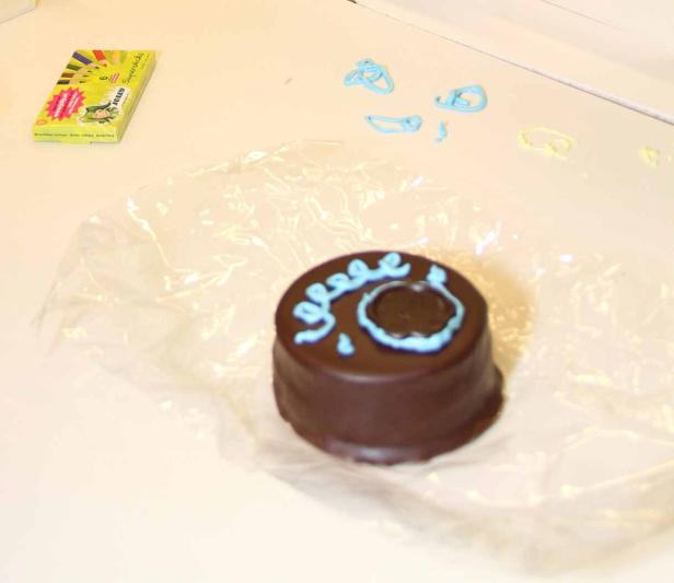 Ein Schokoladenkuchen mit blauer Zuckergussbeschriftung liegt auf einer Plastikfolie.