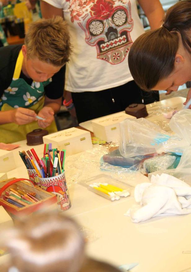 Kinder verzieren kleine Holzkisten mit Stiften und Dekorationen.