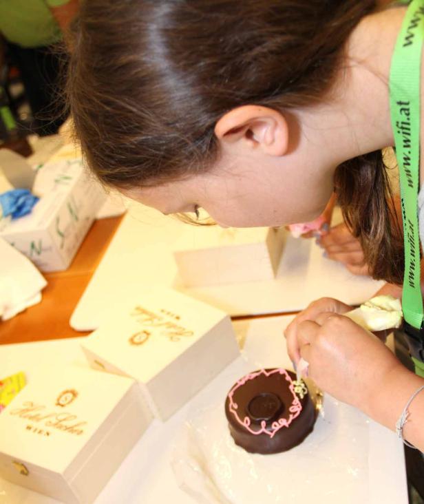 Eine junge Frau verziert eine Sachertorte mit rosa Zuckerguss.