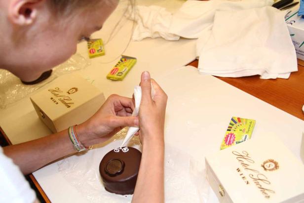 Eine Frau verziert eine Mini-Sachertorte mit Zuckerguss.
