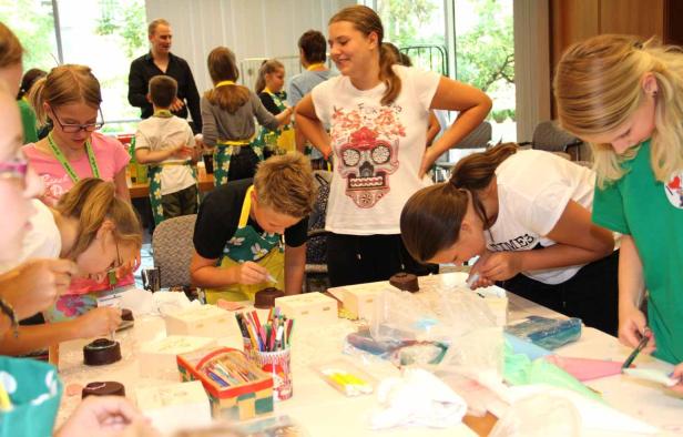 Eine Gruppe Kinder verziert Kuchen und kleine Holzkisten an einem Tisch.