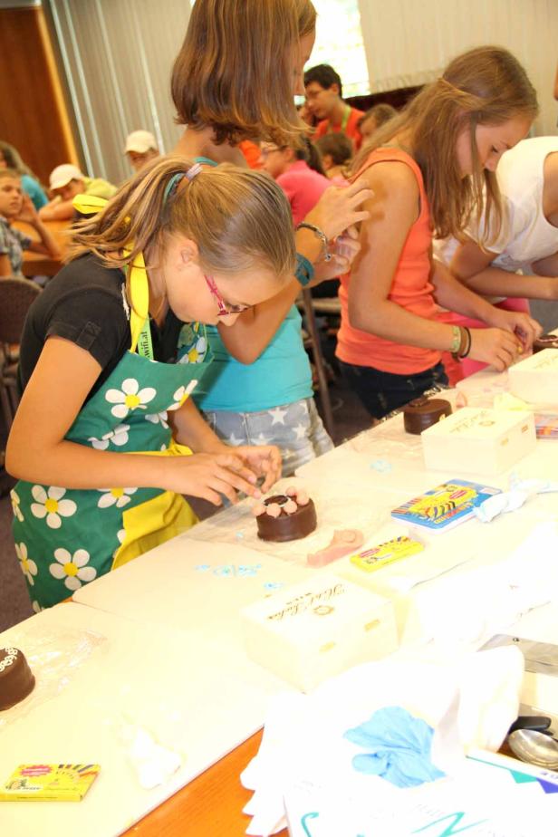 Mehrere Mädchen verzieren kleine Schokoladenkuchen mit Dekorationen.