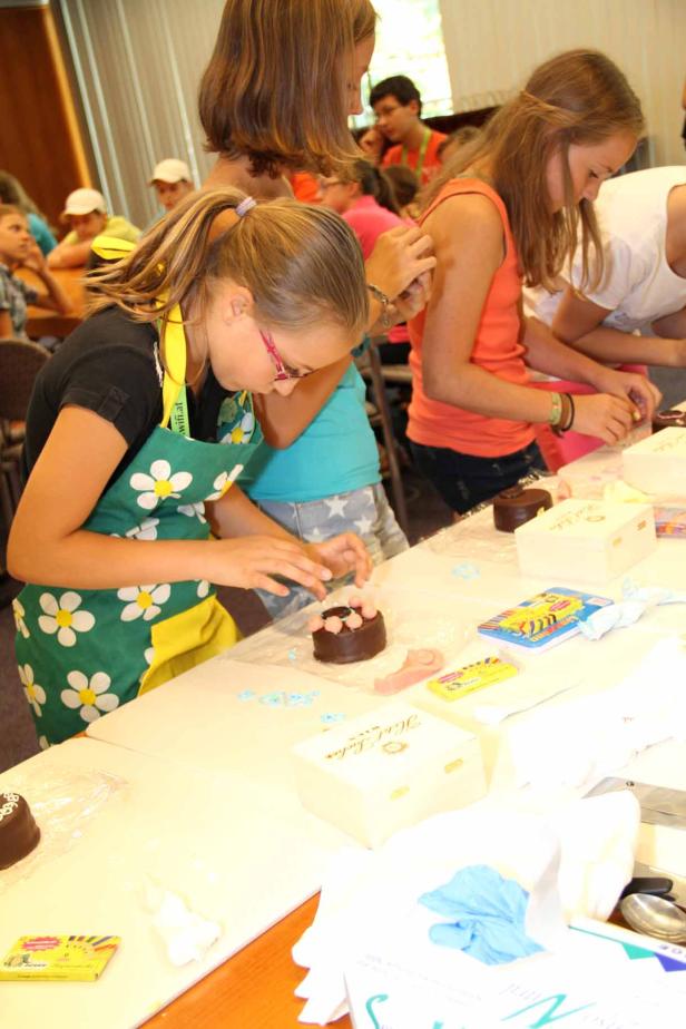 Mehrere Kinder verzieren kleine Schokoladenkuchen mit Zuckerdekorationen.