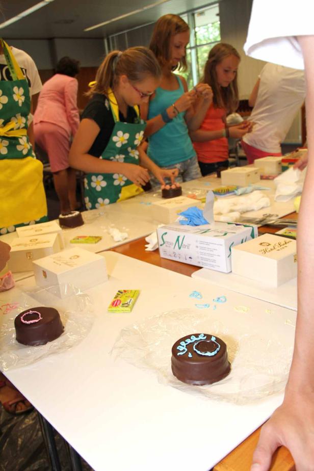 Mehrere Mädchen verzieren Schokoladenkekse an einem Tisch.