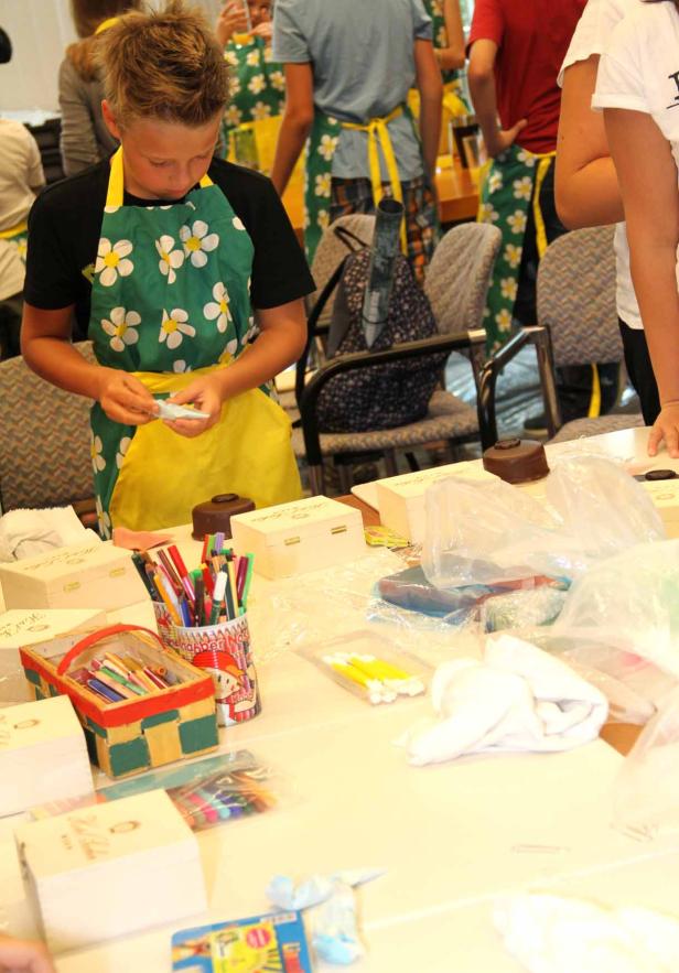 Ein Junge mit Schürze bastelt an einem Tisch mit verschiedenen Materialien.