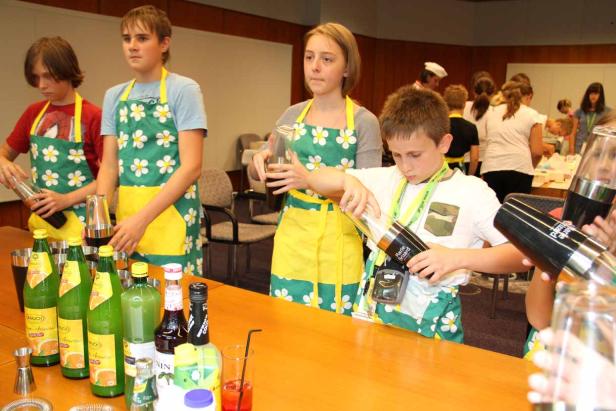 Kinder mixen Cocktails in einer Bar mit Schürzen und Shakers.