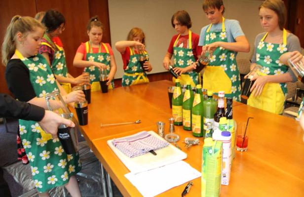 Eine Gruppe von Kindern mixt Cocktails in Schürzen mit Blumenmuster.