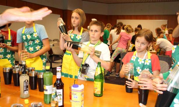 Kinder mixen Cocktails in Schürzen mit Blumenmuster.